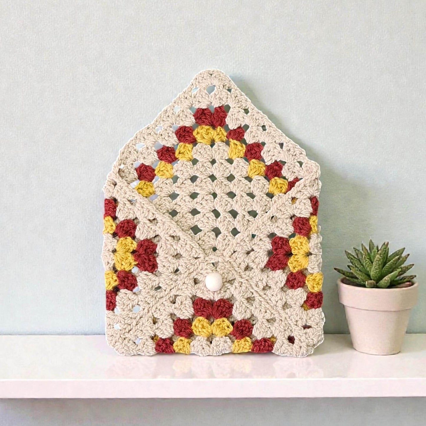 Husă de carte croșetată handmade cu model triunghiuri colorate crem, roșu burgund și galben, unicat, ideală pentru iubitorii de lectură și cadouri originale în România.