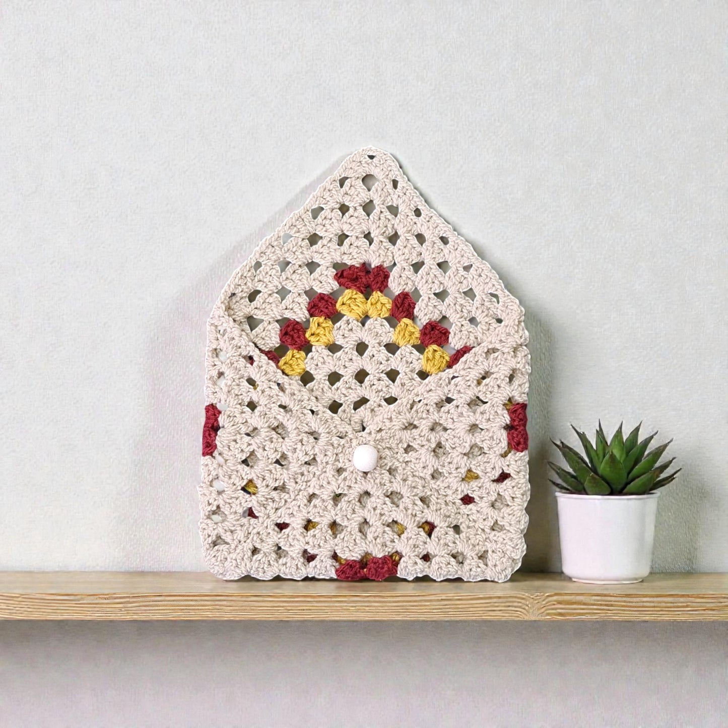 Husă croșetată manual, model romb colorat, oferă protecție delicată pentru carte, agendă sau tabletă mică.